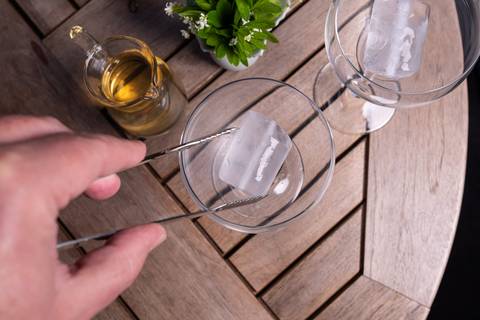 Eiswürfel wird mit einer Zange in ein Bowleglas gelegt