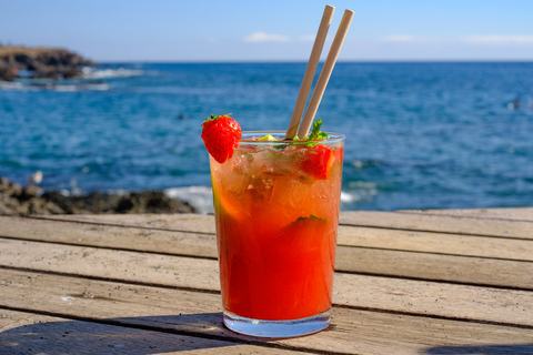 Erdbeerbowle im breiten Longdrinkglas auf Holzdeck, mit Schattenwurf, vor blauem Meer und Himmel – Sommergenuss pur
