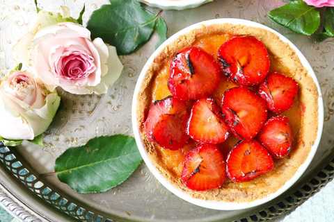 Erdbeertarte mit halbierten Erdbeeren, daneben Rosen