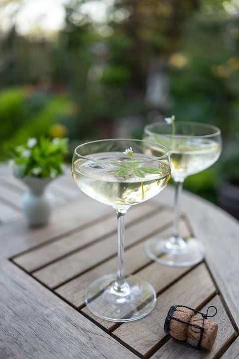 Waldmeisterbowle im Glas mit Eiswürfeln und Dekoration im Garten serviert